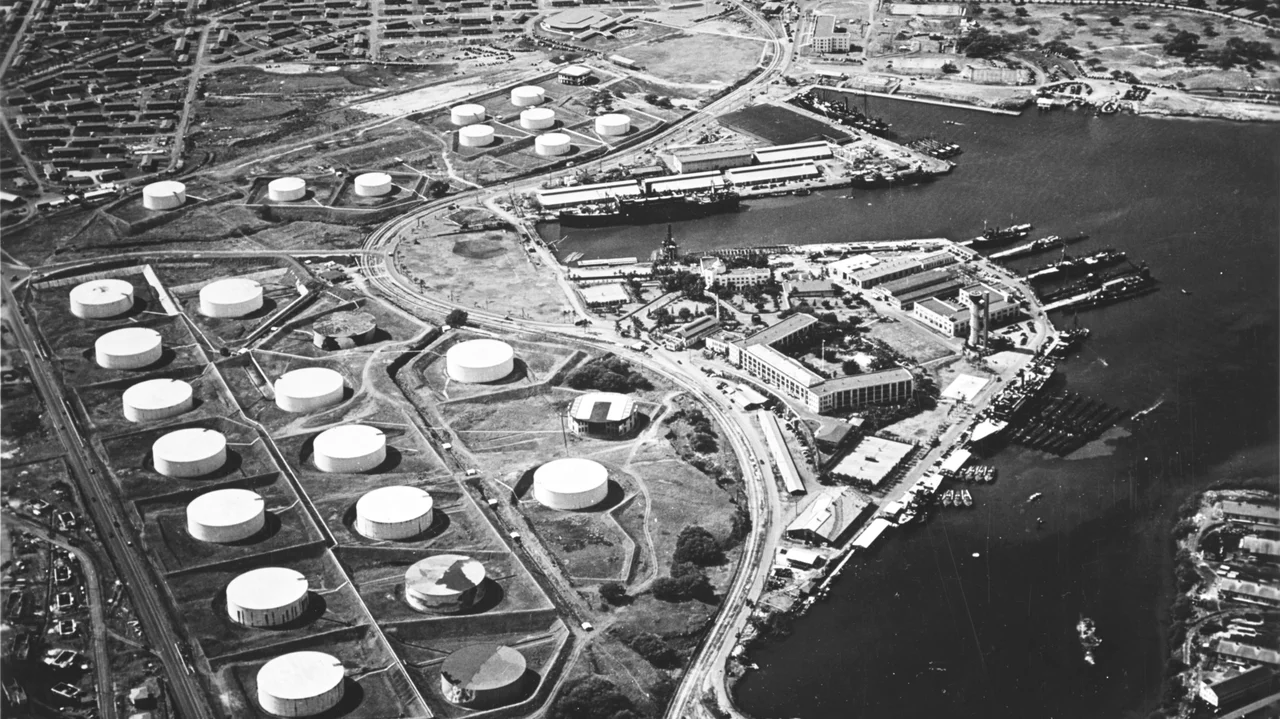 Aerial view of the Pearl Harbor submarine base (right center) with the fuel farm at left, looking south on 13 October 1941.
Among the 16 fuel tanks in the lower group and ten tanks in the upper group are two that have been painted to resemble buildings (topmost tank in upper group, and rightmost tank in lower group). Other tanks appear to be painted to look like terrain features.
Alongside the wharf in right center are USS Niagara (PG-52) with seven or eight PT boats alongside (nearest to camera) and USS Holland (AS-3) with seven submarines alongside. About six more submarines are at the piers at the head of the submarine base peninsula.